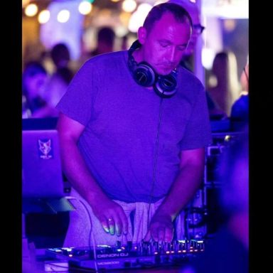 DJ bei Nachtveranstaltung, konzentriert am Mischpult, mit Kopfhörern und bunten Lichtern.